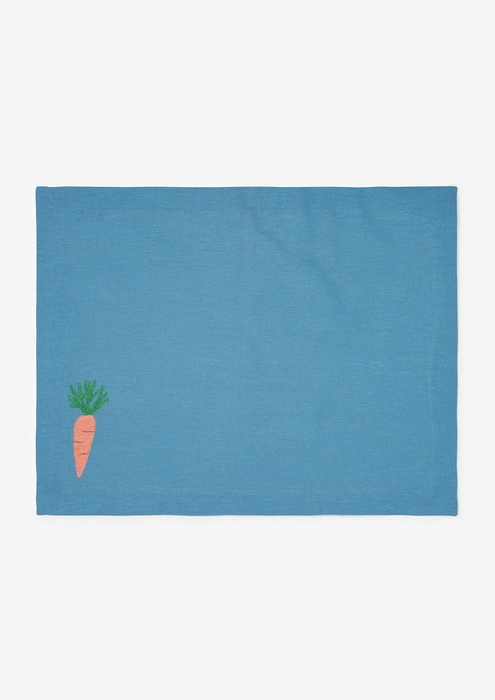 A blue cotton placemat with carrot embroidery at bottom left corner.