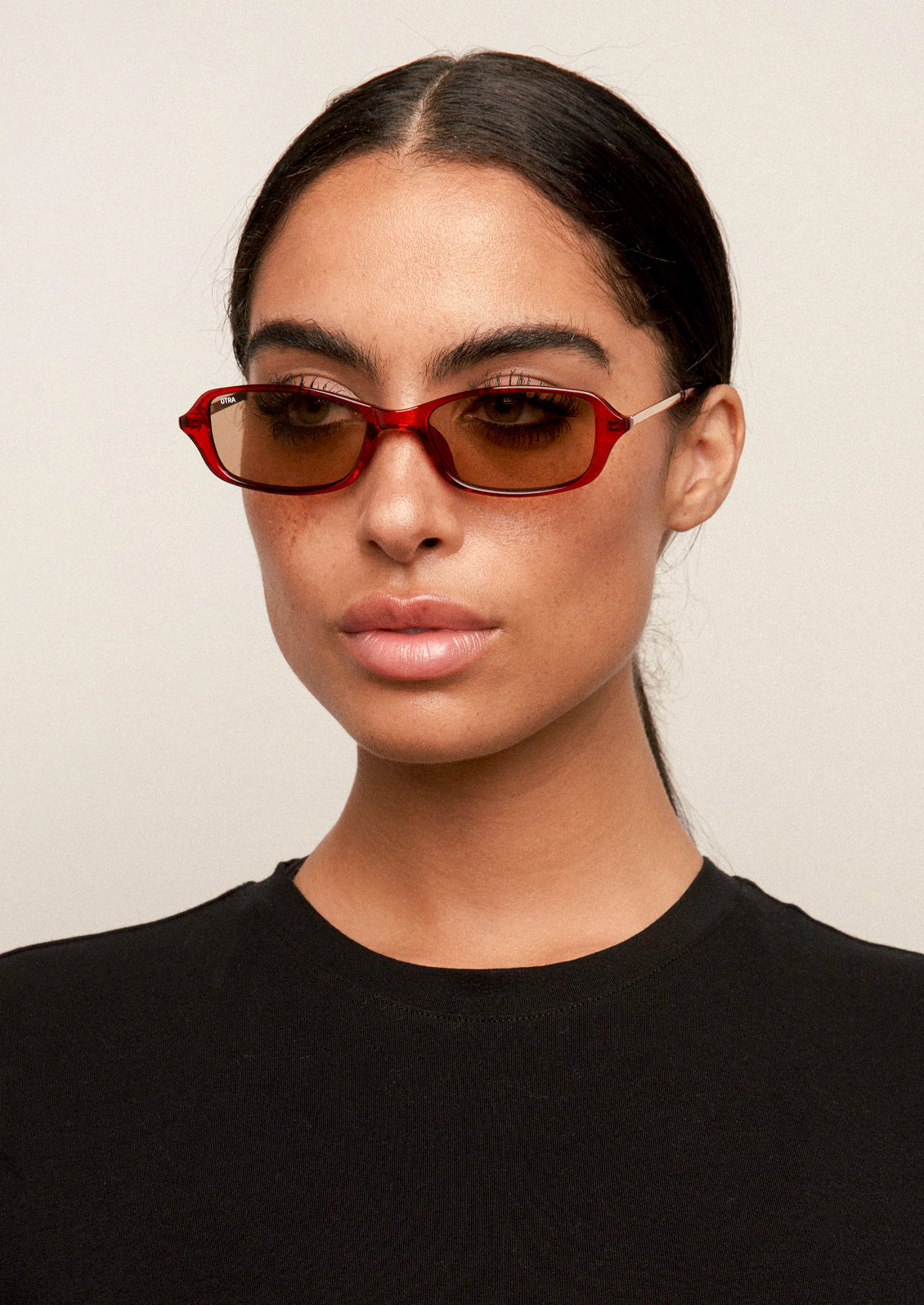 A woman wearing a pair of square sunglasses with a cherry brown frame and brown lenses.