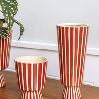 2: A tall and skinny vase with conical shape in red ceramic with vertical thin white stripes.