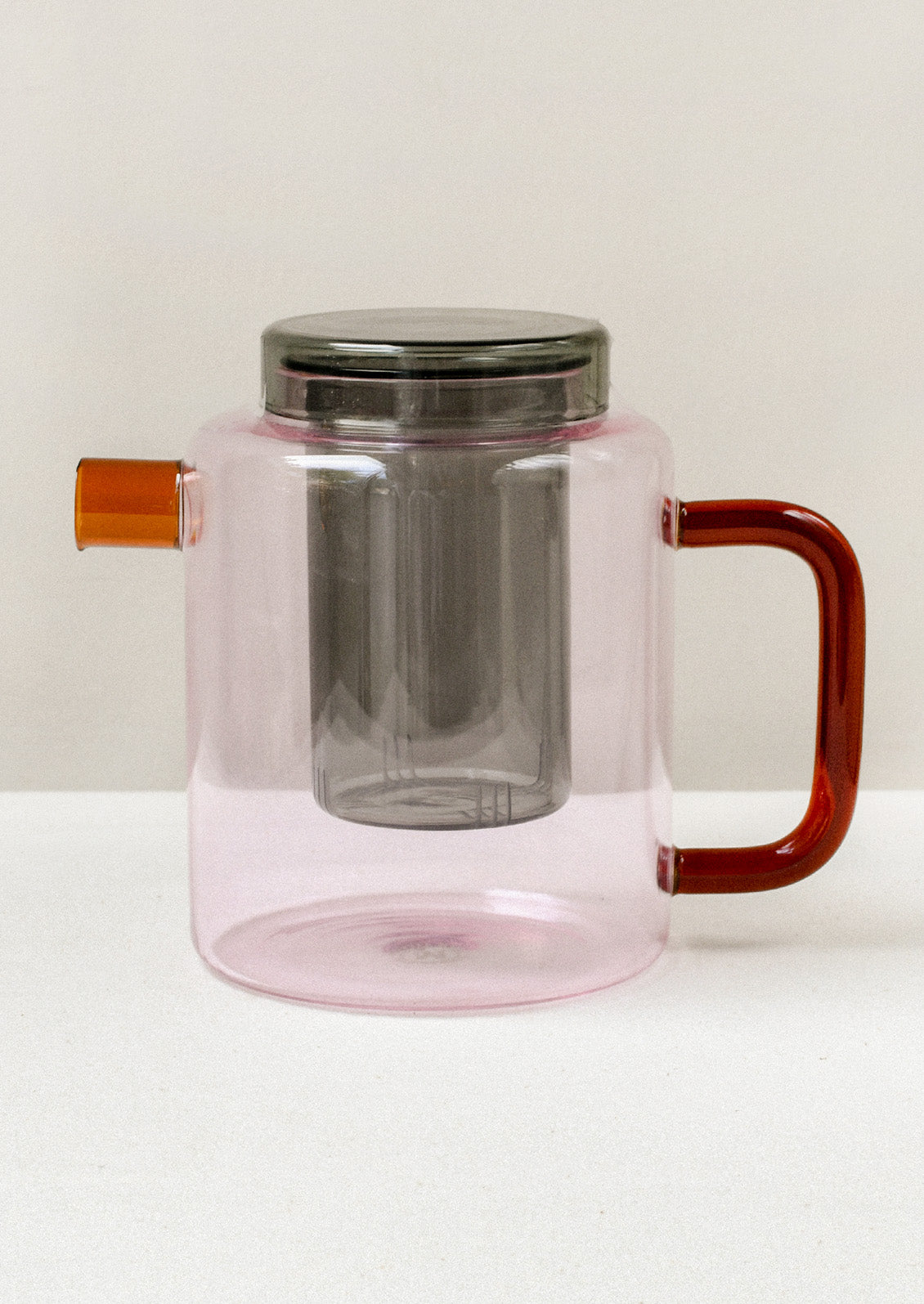 A multicolored glass teapot with a pink body, orange spout, red handle, and removable grey tea steeper.