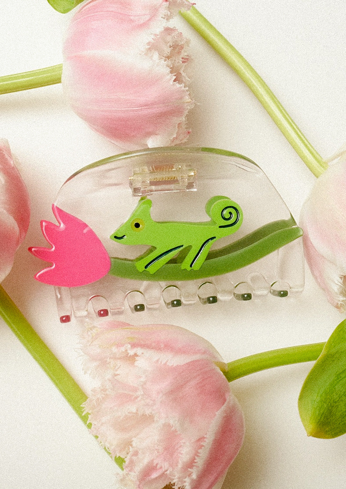 A clear claw clip with a green chameleon and pink tulip on a white background surrounded by pink flowers.