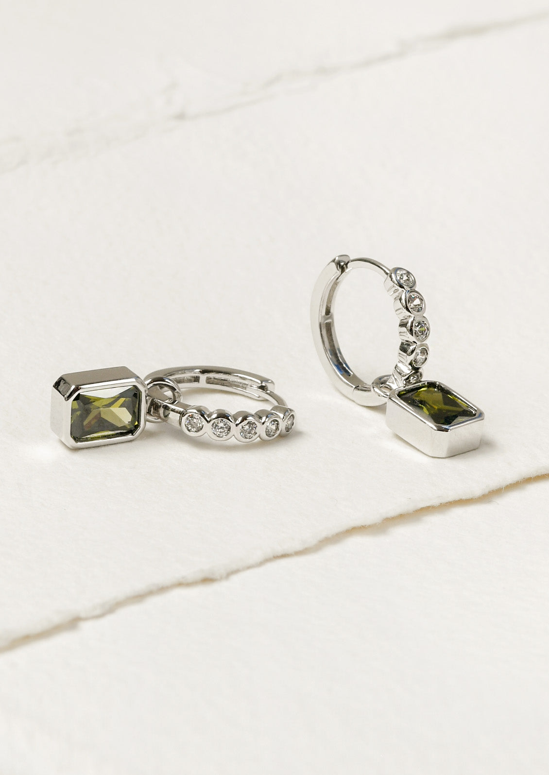 A pair of silver hoop earrings adorned with white crystals and dangling green gemstones.