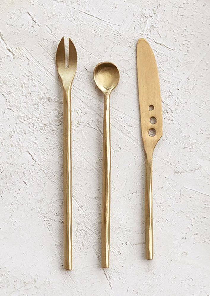 A set of three brass cheese utensils (knife, spoon and fork) in modern shape.