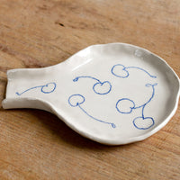 2: A handmade ceramic spoon rest with hand-drawn cherries in blue.