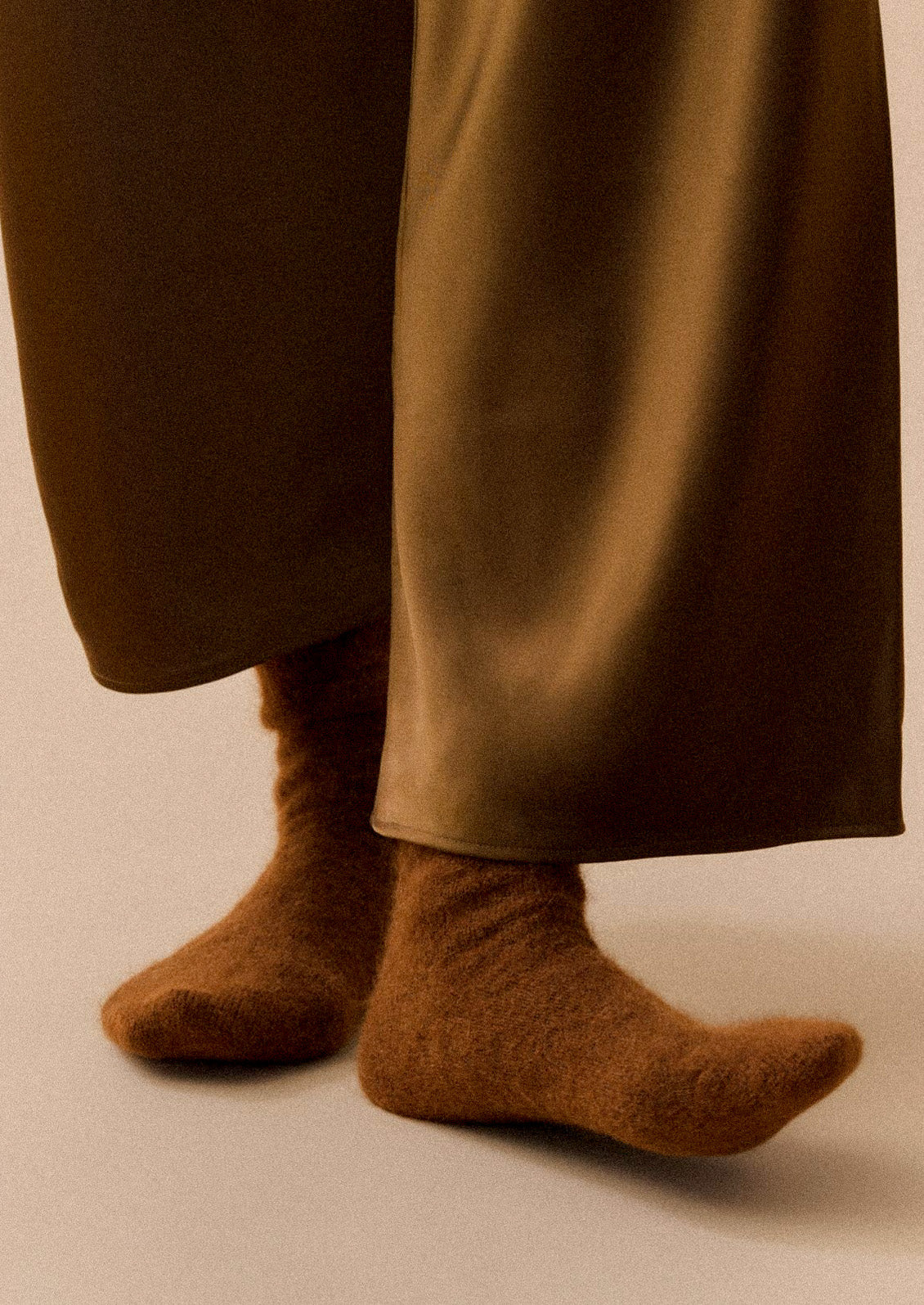 A person wearing brown wide leg pants and brown textured alpaca blend socks.