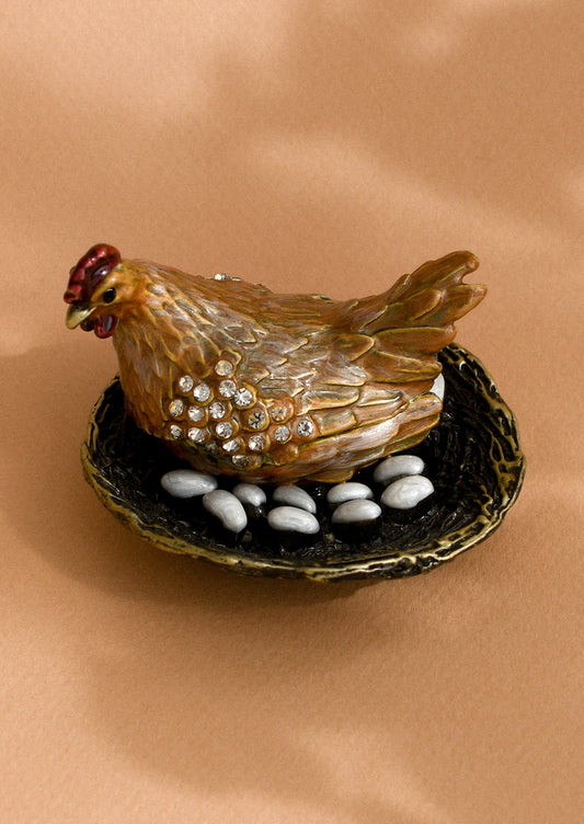 A crystal detailed metal trinket box depicting a chicken laying on eggs.