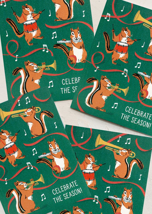 A set of green greeting cards with illustration of chipmunks playing musical instruments, text reads "Celebrate the season".