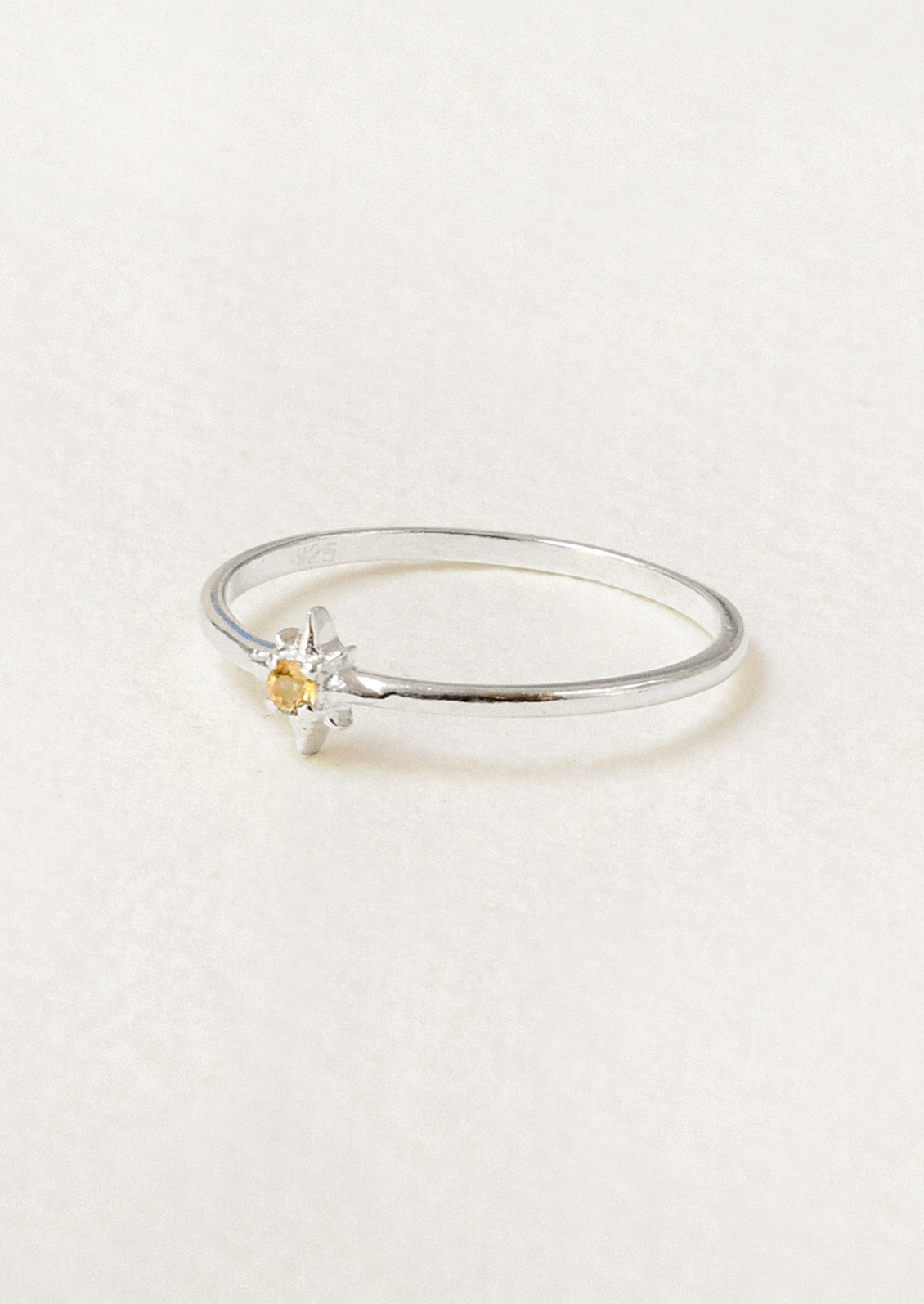 Side view of a sterling silver ring with a thin band and a citrine stone in the center set in a starburst design.