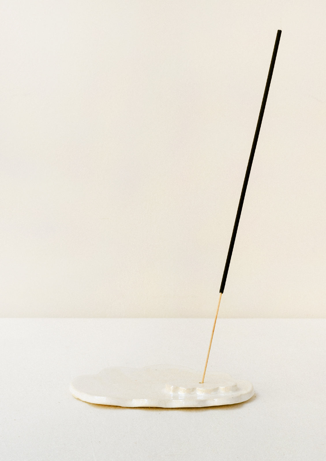A white ceramic iridescent cloud-shaped incense holder with an incense stick.
