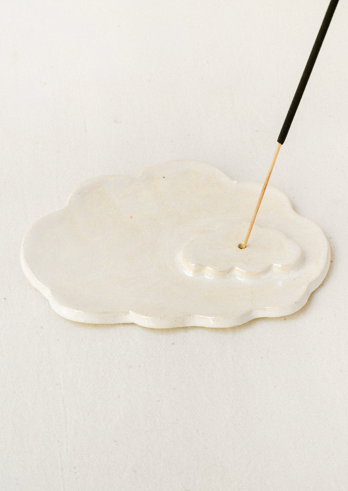 A white ceramic iridescent cloud-shaped incense holder with an incense stick.