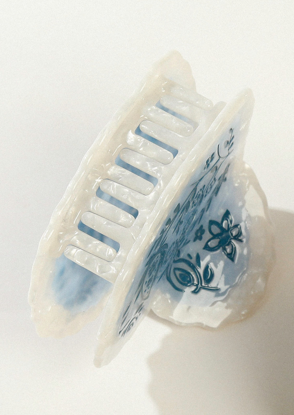 A large heart shaped hair claw with a pearlescent border and a blue floral design in the middle.
