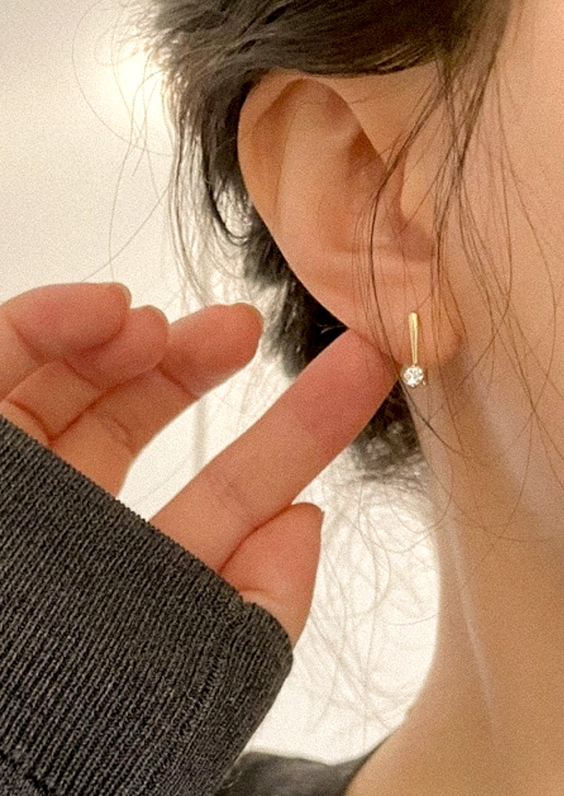 A woman wearing a gold hook earring with a cubic zirconia solitaire gem.
