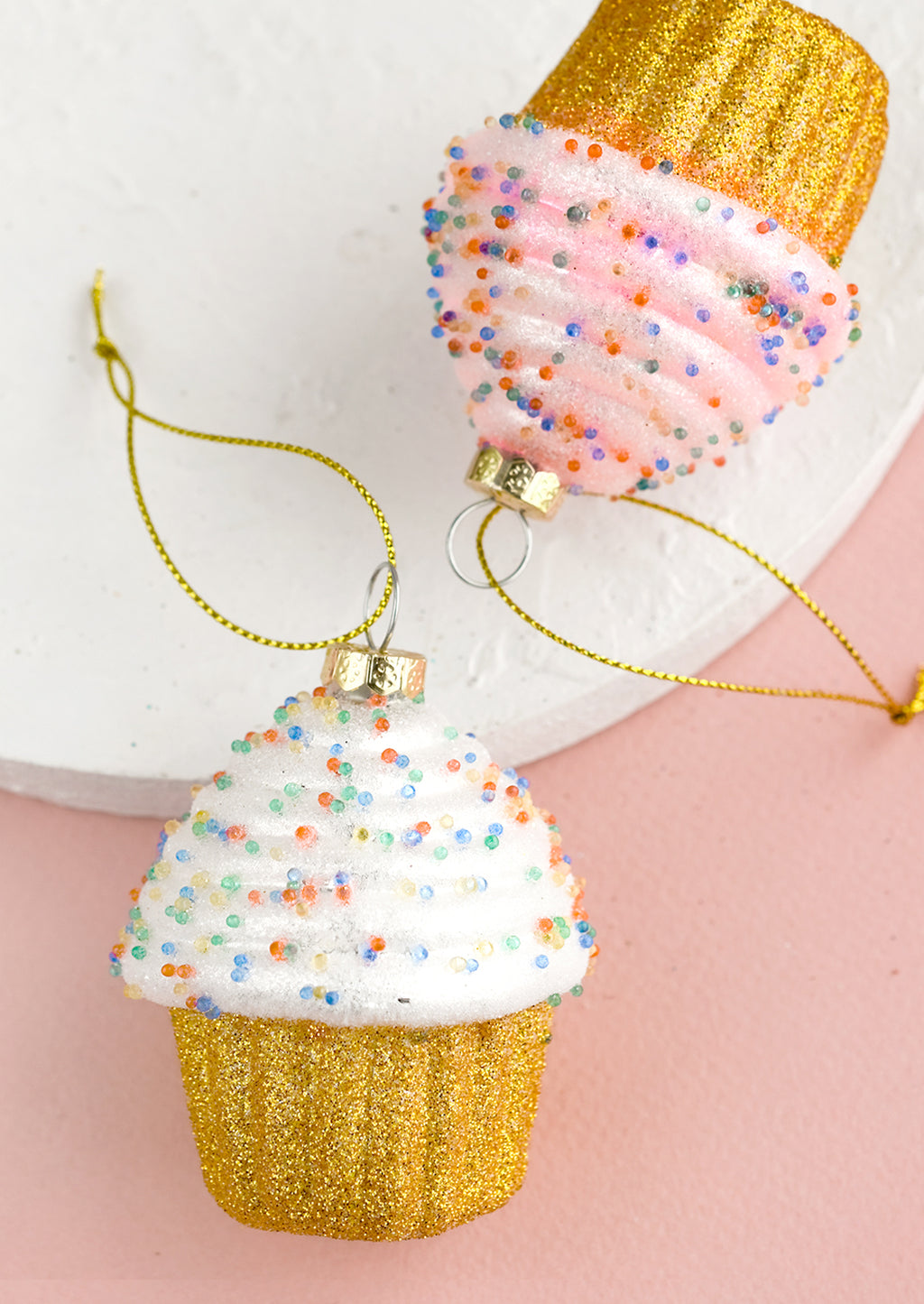 2: Glass ornaments of frosted, sprinkled cupcakes in white and pink.
