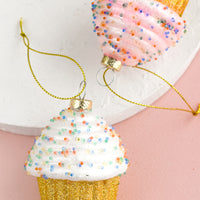 2: Glass ornaments of frosted, sprinkled cupcakes in white and pink.