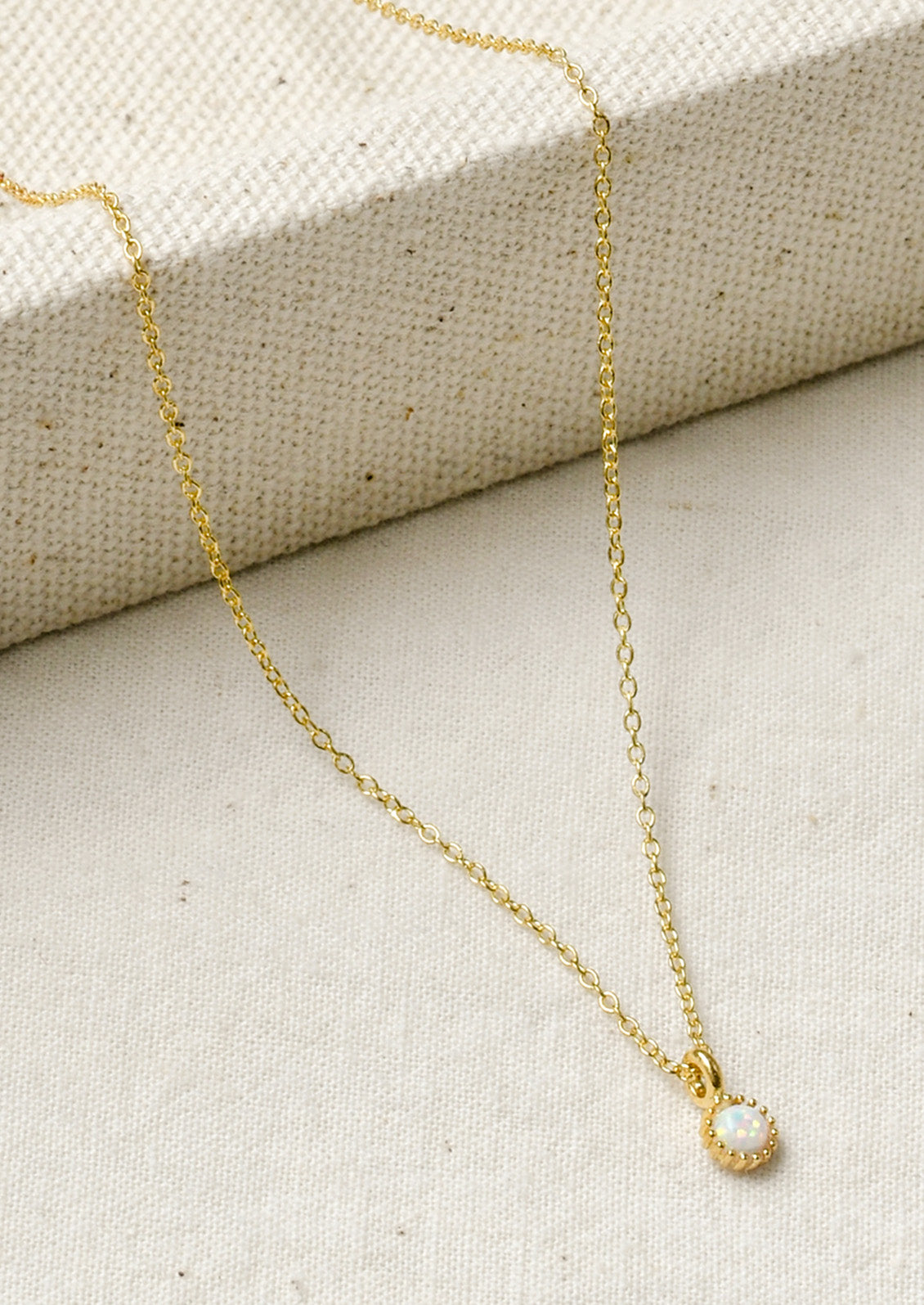 A dainty gold necklace with a small simulated opal charm.