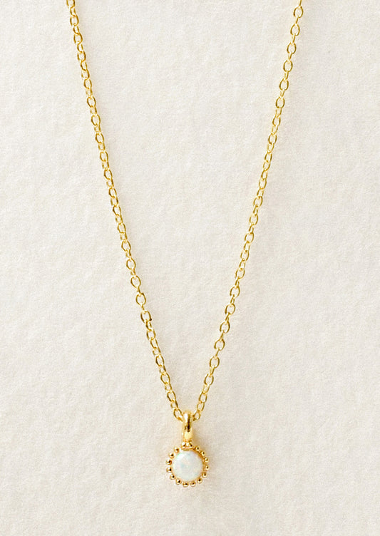 A dainty gold necklace with a small simulated opal charm.