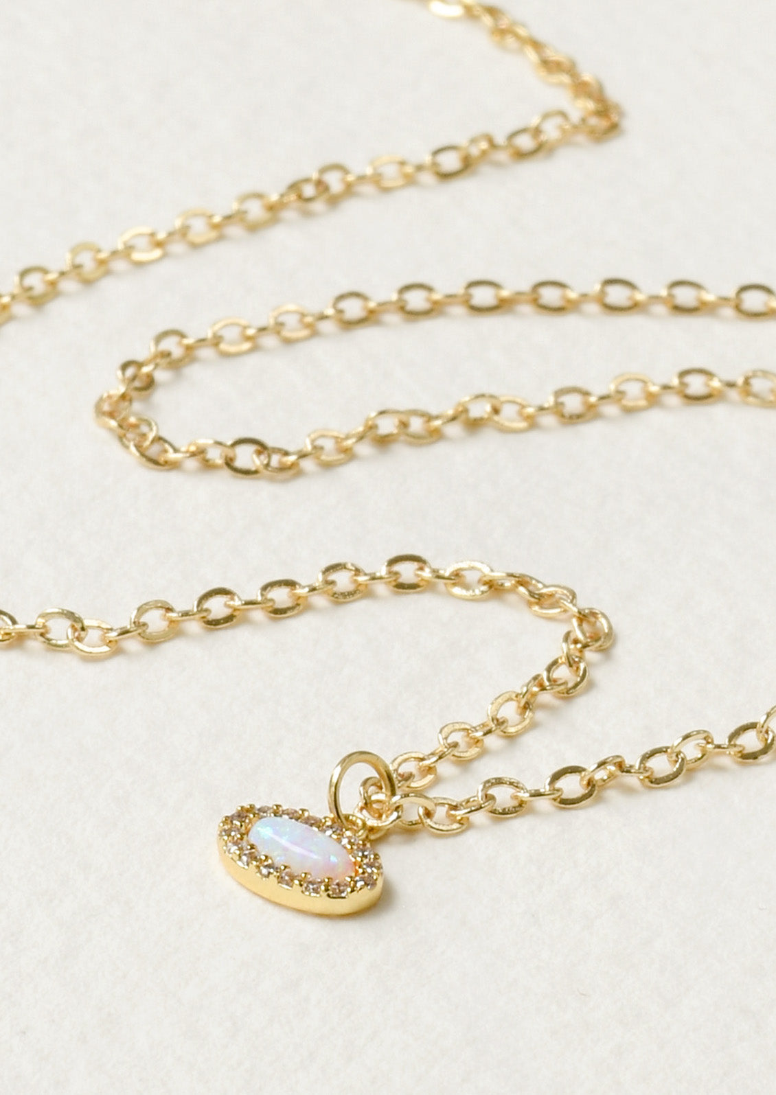 A delicate and dainty gold necklace with a small oval opal charm surrounded by tiny cubic zirconia.