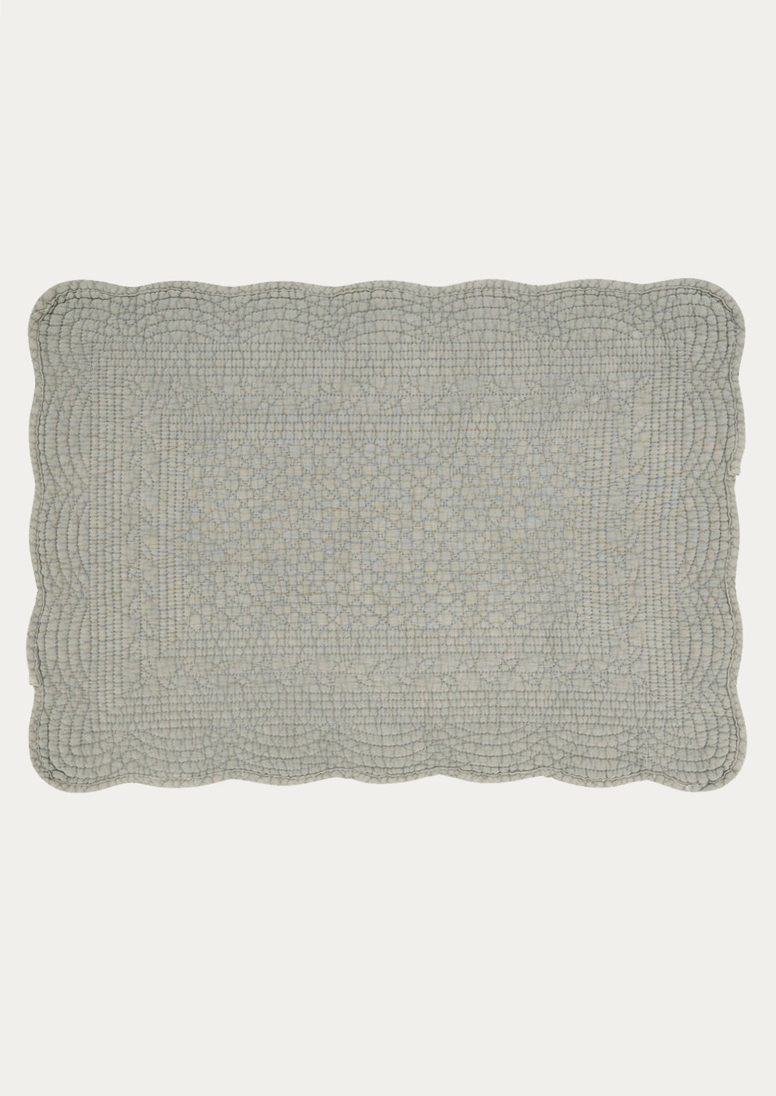 A quilted cotton placemat with scalloped edges, in blue-grey color.