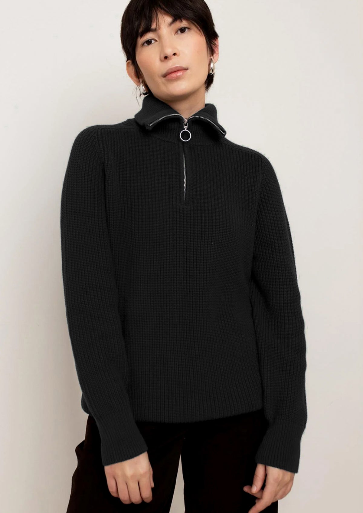 A person wearing a black sweater with silver zip at funnel neck.