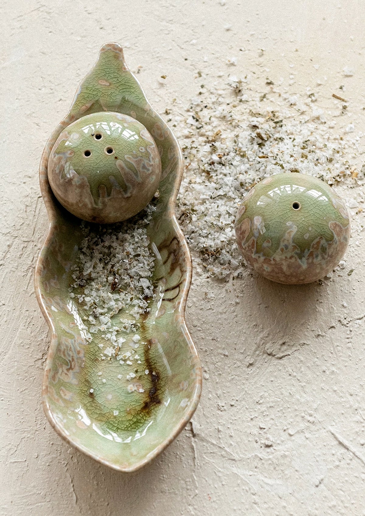 A set of round shakers with tray resembling a pea pod.