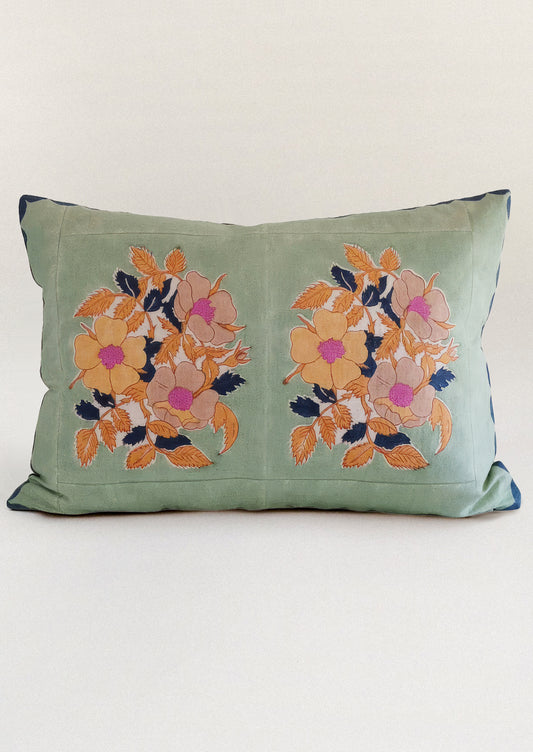 A block printed throw pillow in mint green with orange floral print.