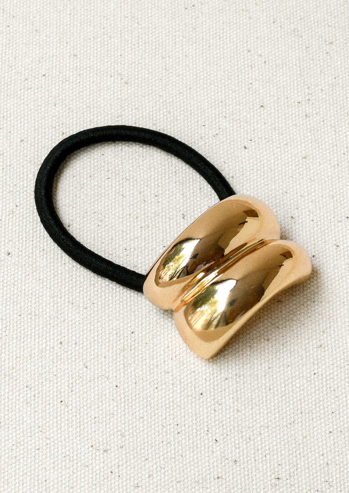 A black elastic hair tie with a gold metal pendant with a double arch design.