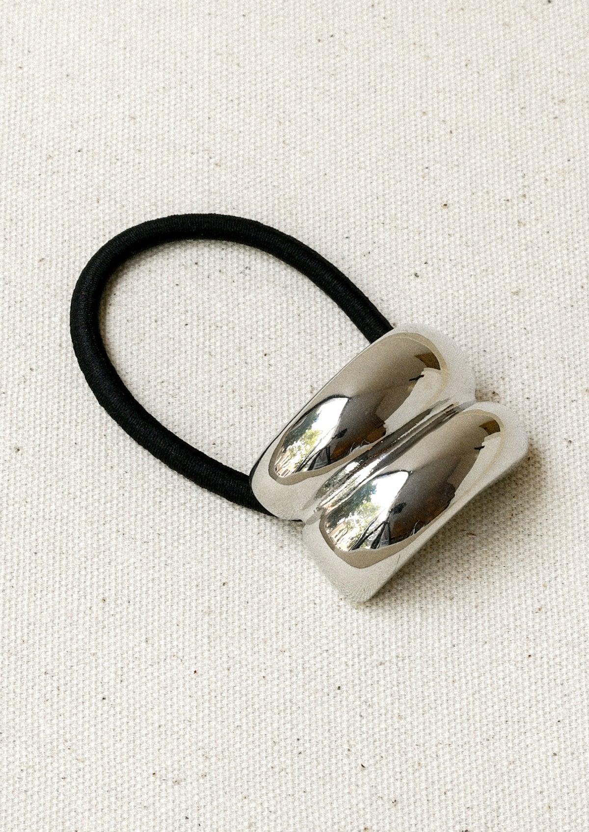 A black elastic hair tie with a silver metal pendant with a double arch design.