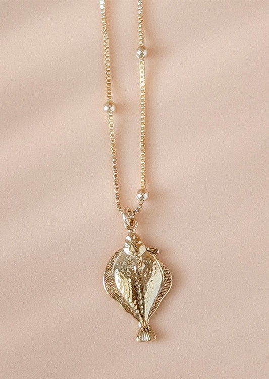 A gold necklace with fish pendant charm.