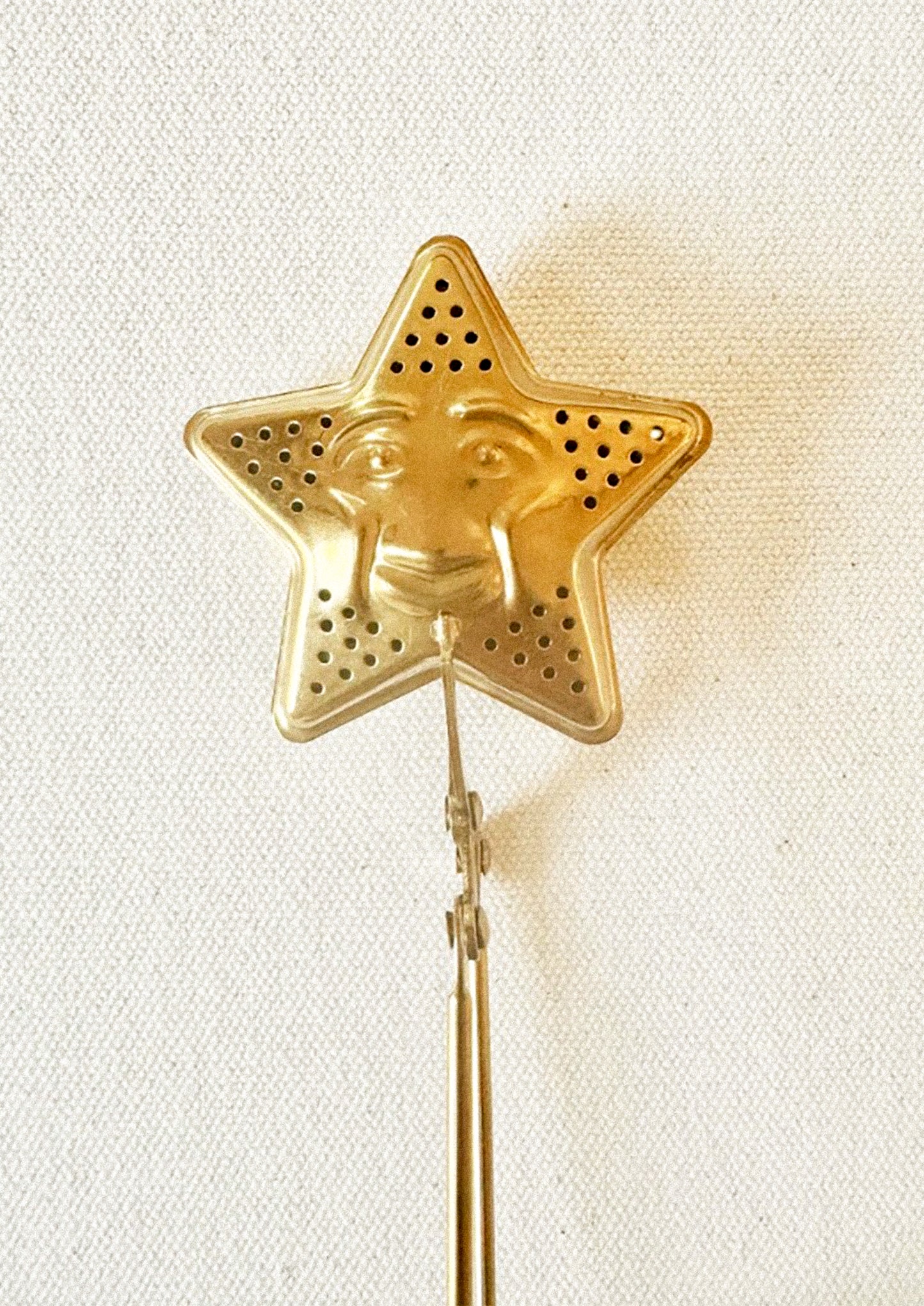 A brass tea steeper with star shaped end with smiling face.