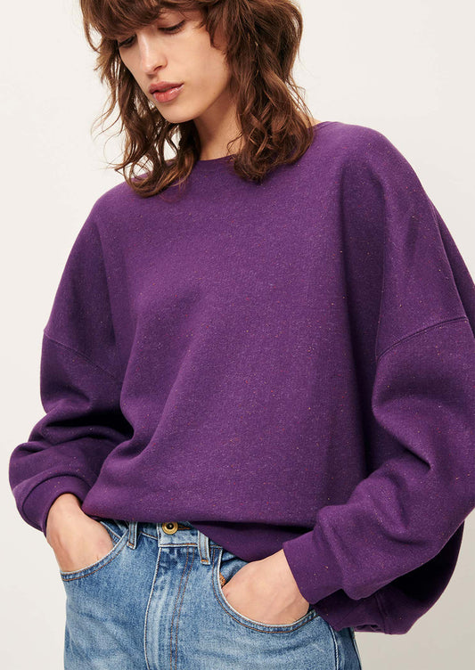 A woman wearing a relaxed fit sweatshirt in vibrant purple with speckles in fabric.