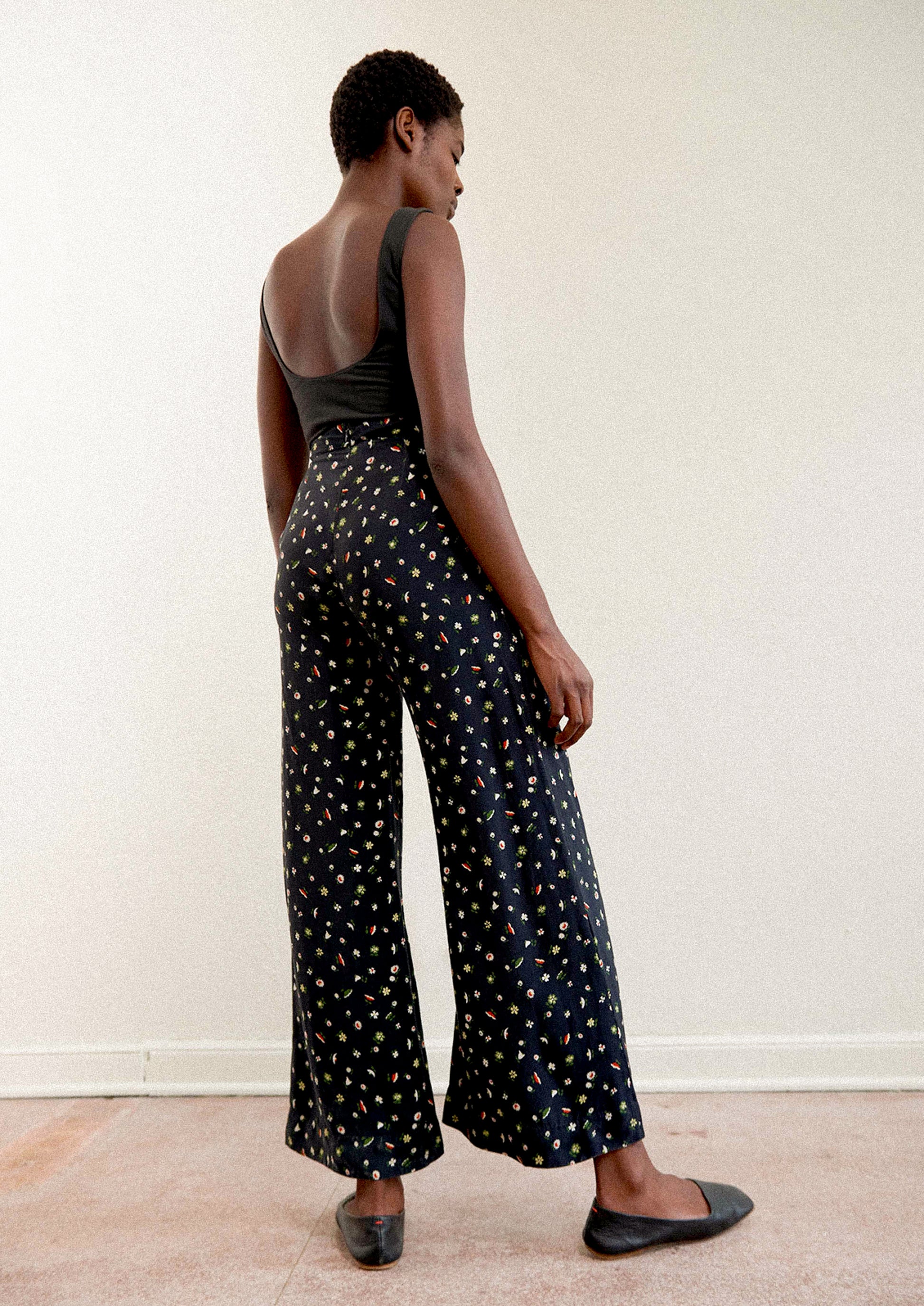 A woman wearing a pair of high waisted pants in black with multicolor botanical print throughout.