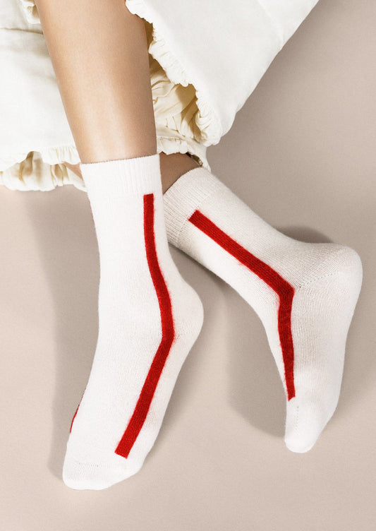 A pair of white cashmere socks with single vertical red stripe.