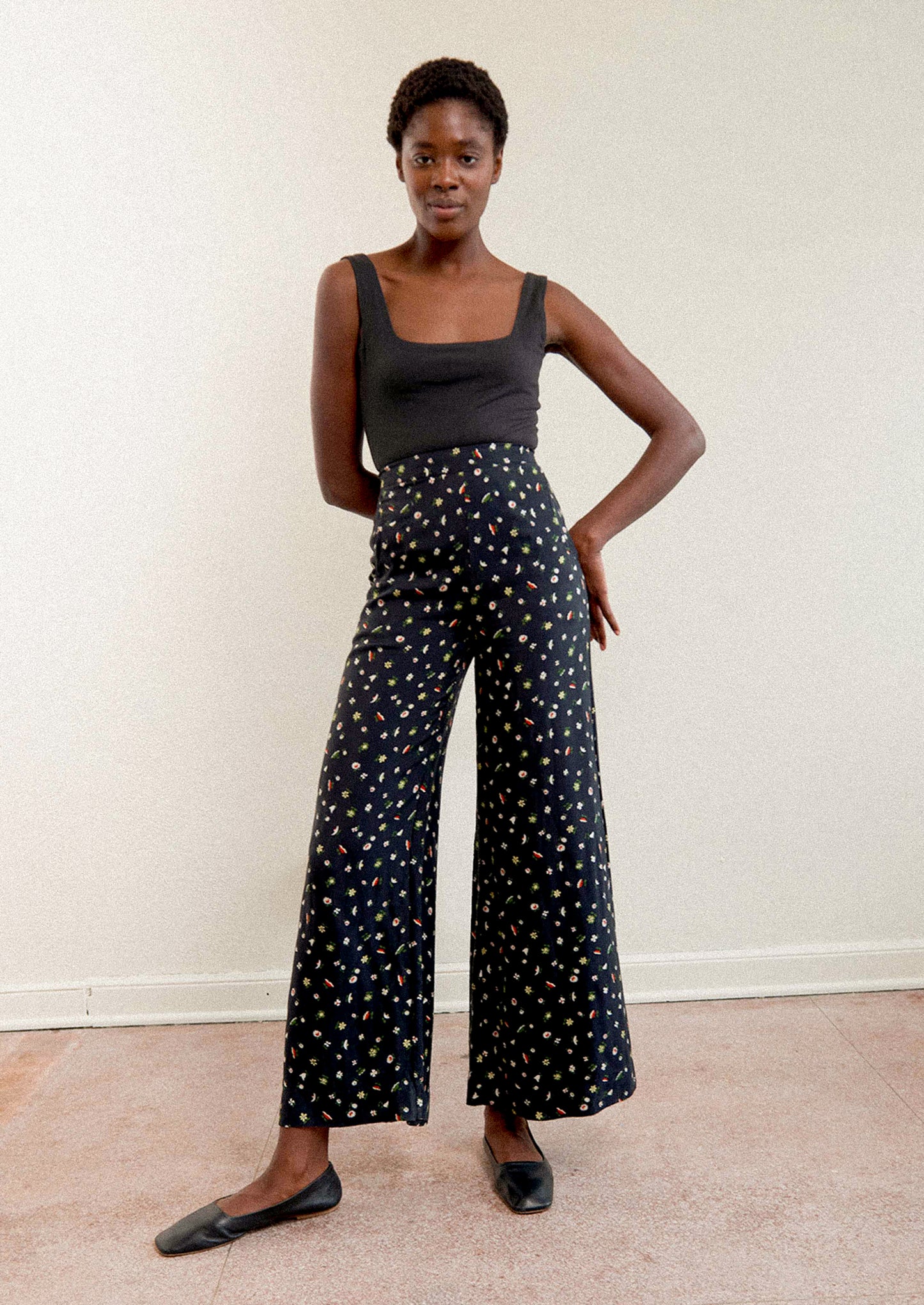 A woman wearing a pair of high waisted pants in black with multicolor botanical print throughout.