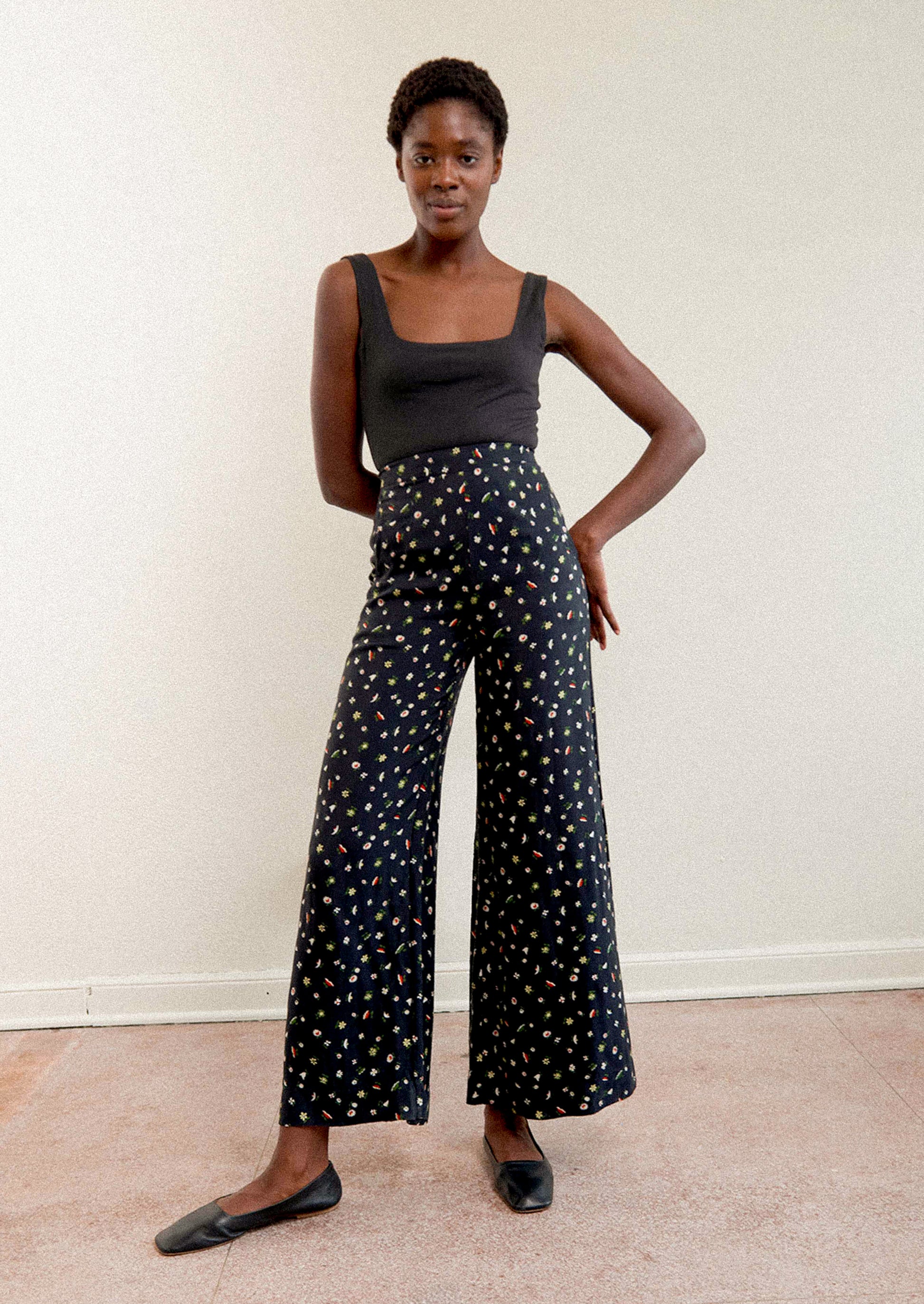 A woman wearing a pair of high waisted pants in black with multicolor botanical print throughout.