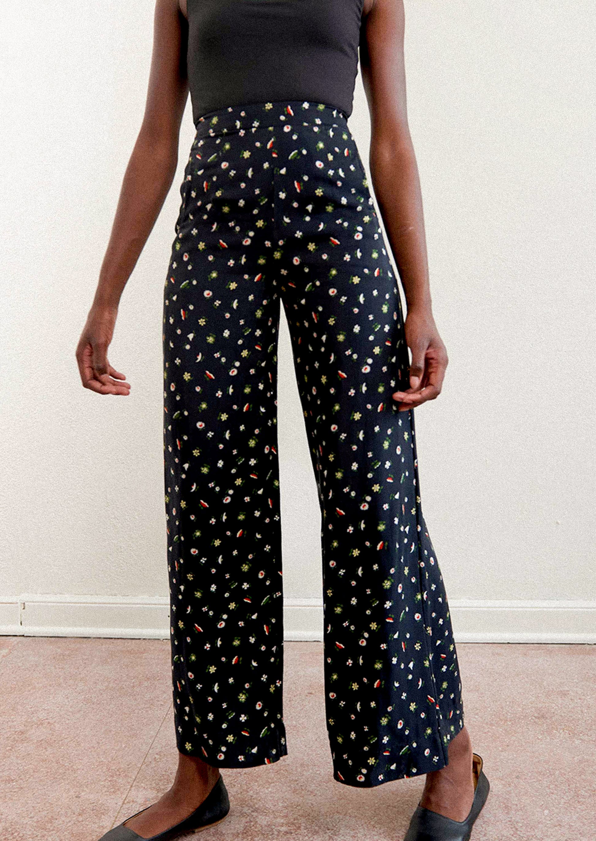 A woman wearing a pair of high waisted pants in black with multicolor botanical print throughout.