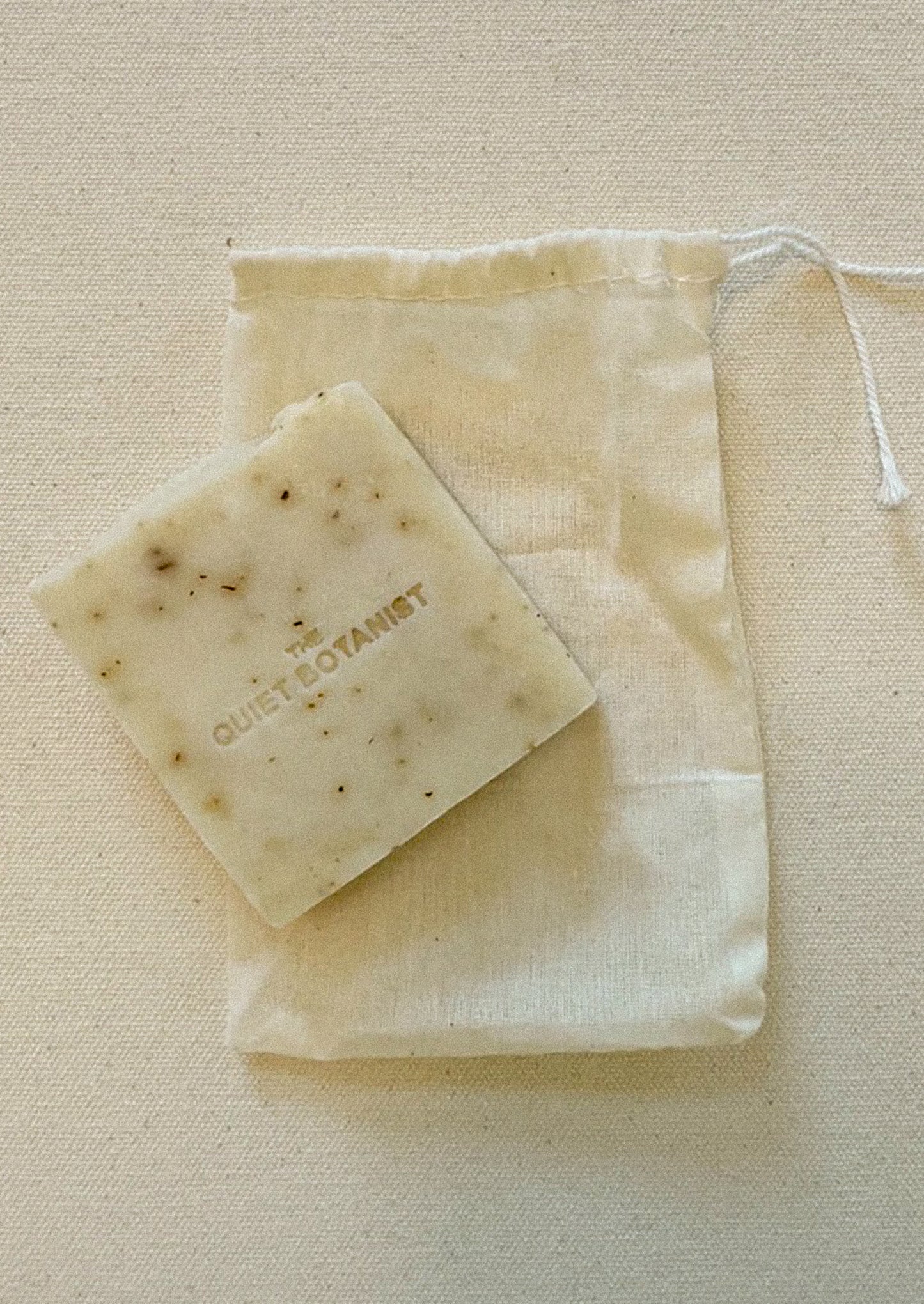 Bar of soap with 'The Quiet Botanist' branding on a beige fabric background