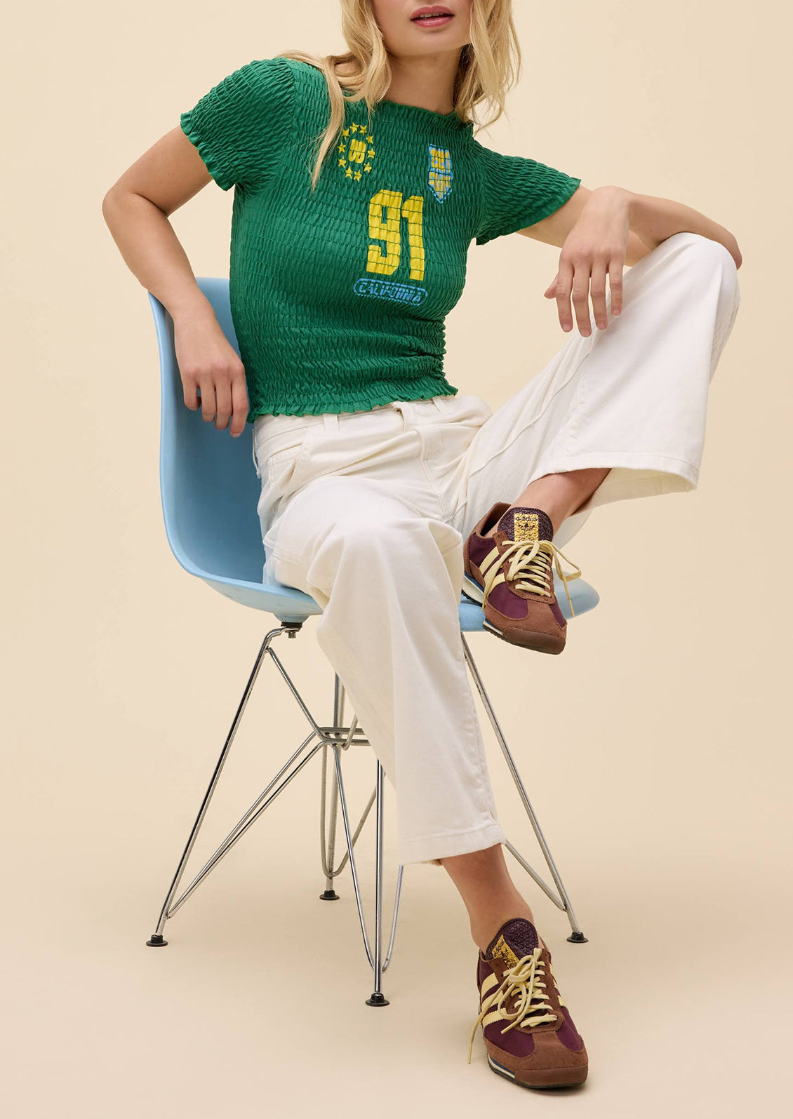 Person wearing a green knitted sweater with a number 91, white pants, and brown shoes sitting on a blue chair.