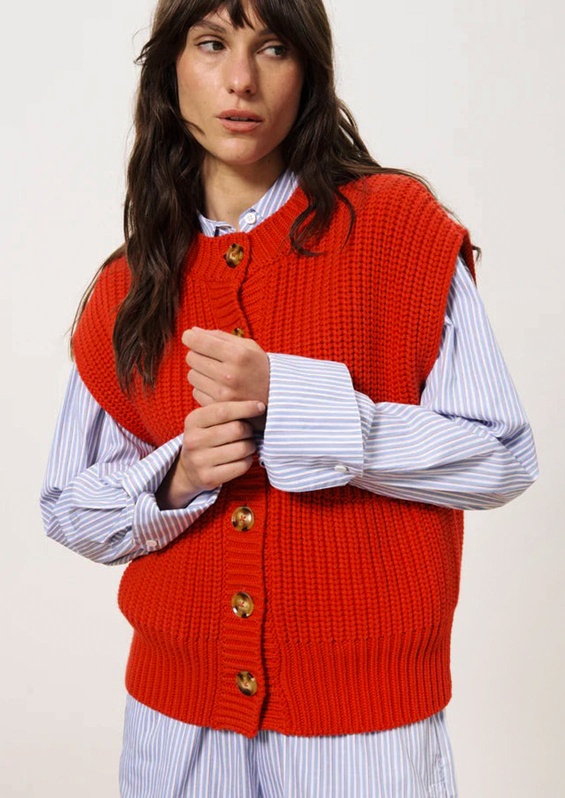 A person wearing a chunky knit button front sleeveless sweater vest in bright cherry red.