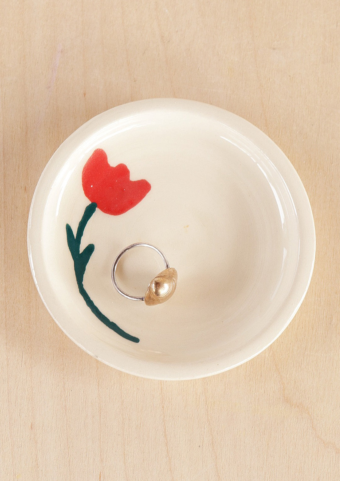 A round ceramic trinket dish in white with hand painted red tulip motif.