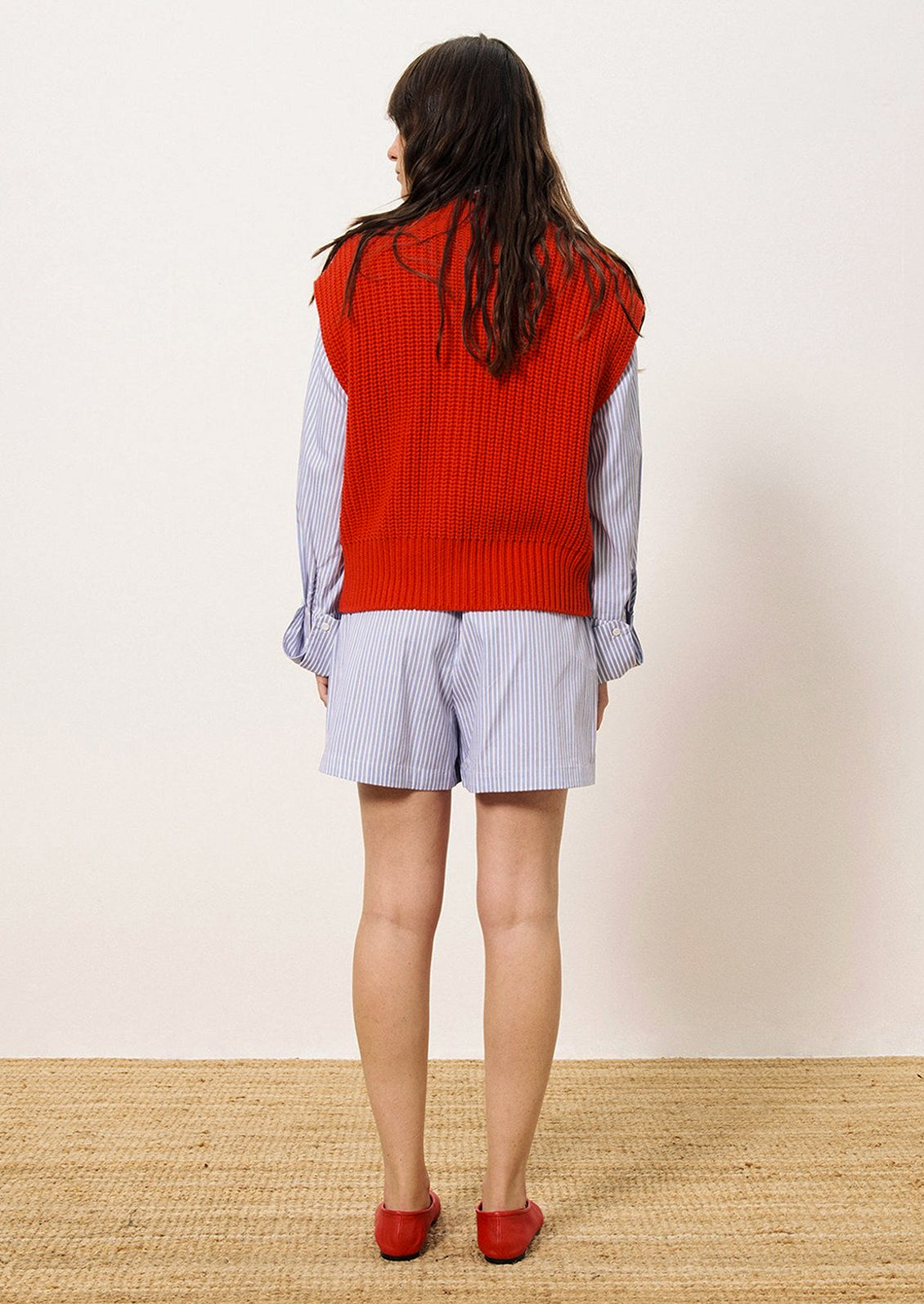 A person wearing a chunky knit button front sleeveless sweater vest in bright cherry red.