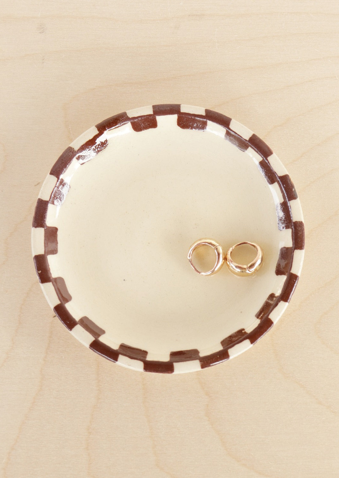 A round ceramic trinket dish with brown checkered border.