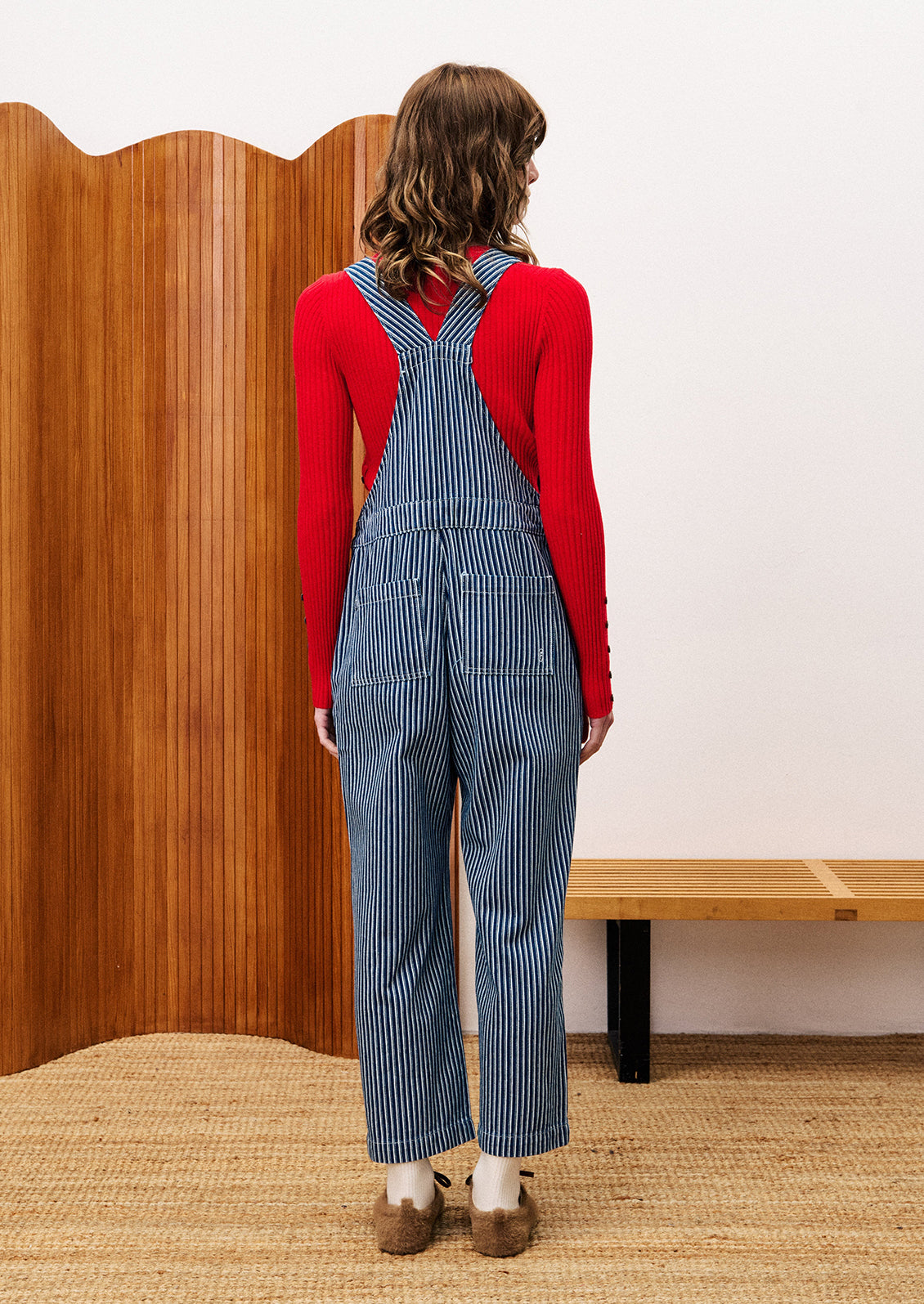 Person wearing a red sweater and blue striped overalls.