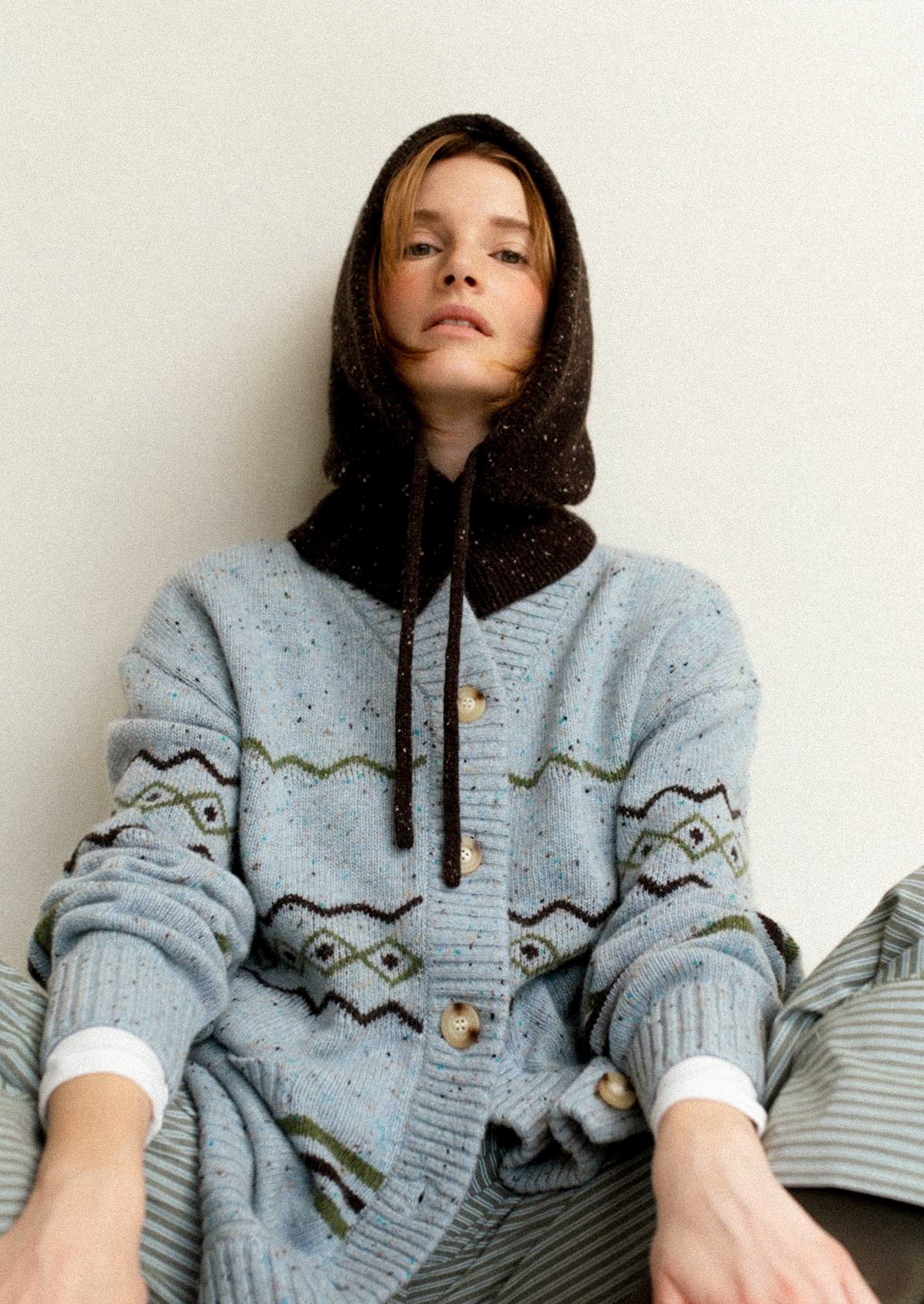 Person wearing a blue patterned cardigan with a hood against a plain background