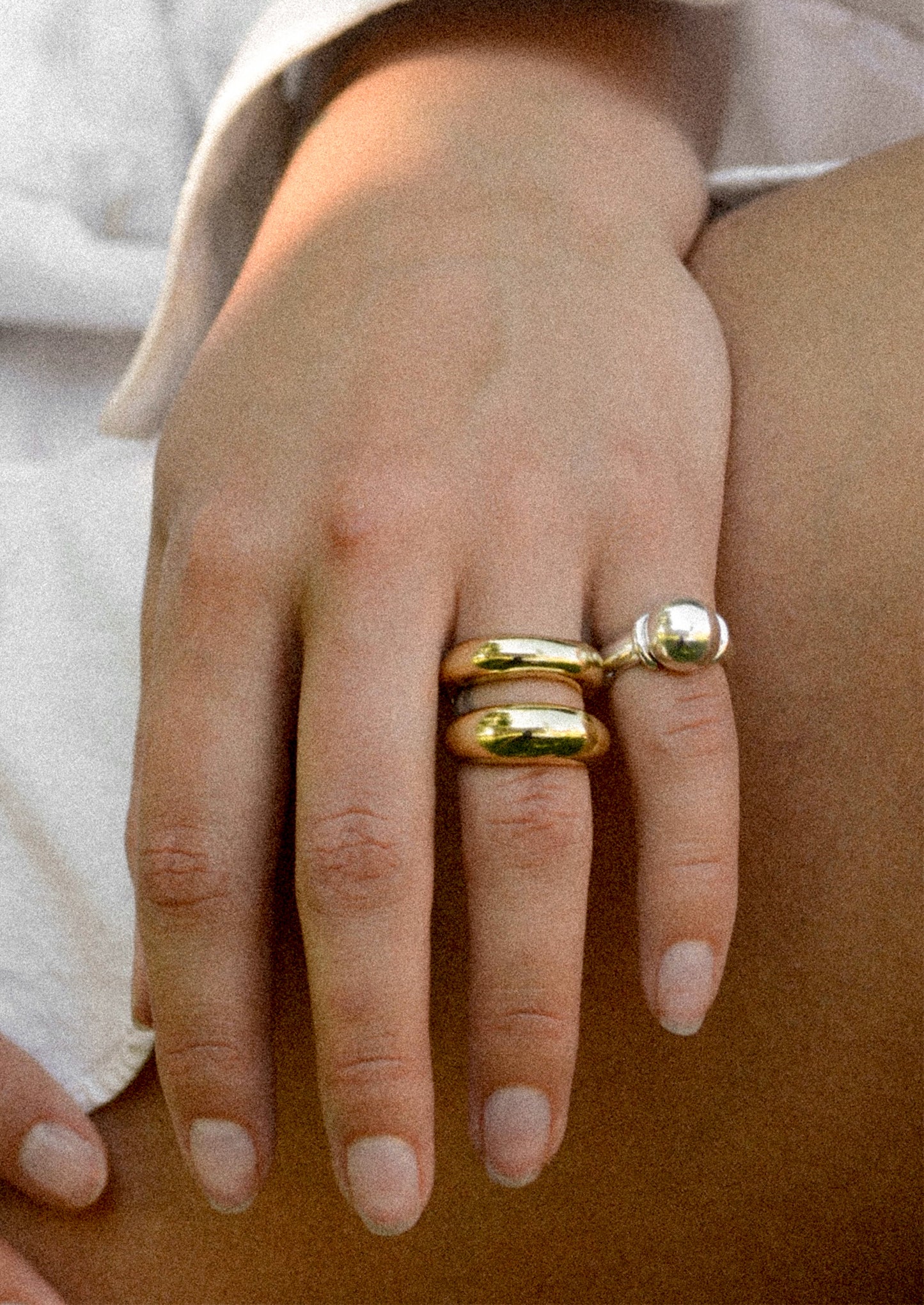 Close-up of a hand wearing two mixed metal rings on a neutral background