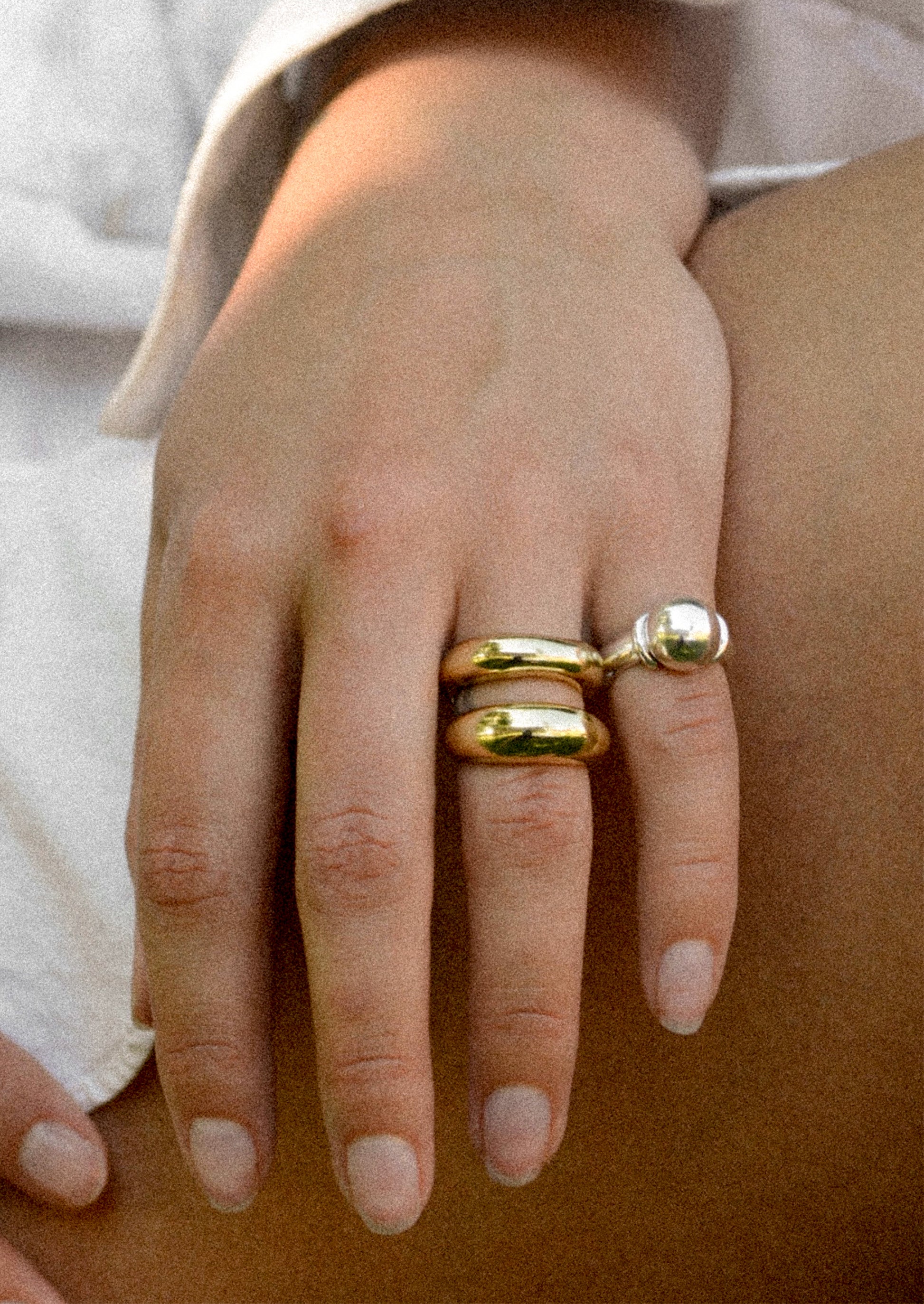Close-up of a hand wearing two mixed metal rings on a neutral background