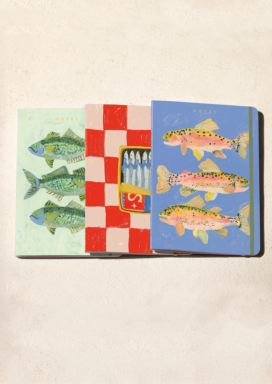 Three notebooks with fish illustrations on a beige background