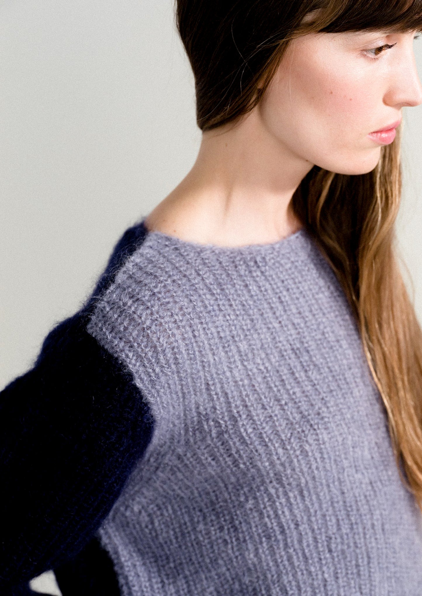 A woman wearing a long sleeve mohair sweater with two-tone colorblocking in dusty blue and navy.