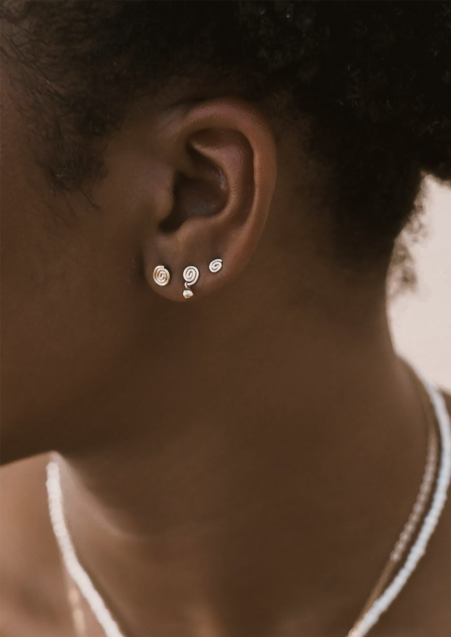 Close-up of a person wearing three pairs of swirl-shaped earrings in different sizes.