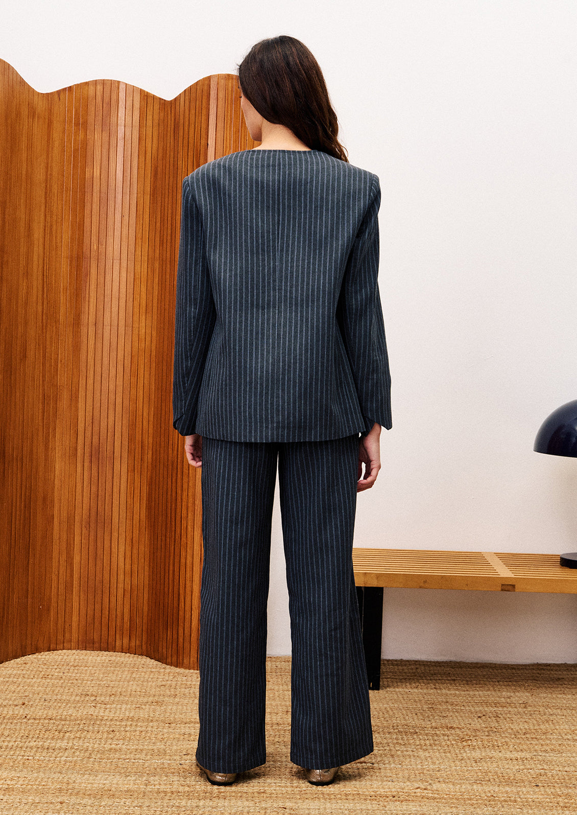 Person wearing a dark pinstripe suit standing in front of a wooden screen.