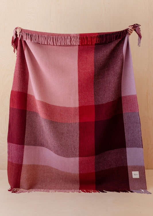 Plaid blanket with red and pink colors draped over a surface against a beige background